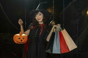 Asian girl in witch costume holding jack'o lantern for halloween party trick or treat concept with dark black background photo