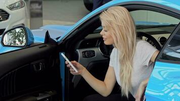 encantador mujer utilizando su inteligente teléfono mientras comprando nuevo coche a el concesión video