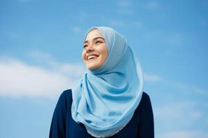 Portrait of beautiful young muslim woman with hijab against blue sky photo