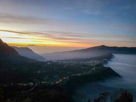 Sunrise view from Penanjakan 2 or Seruni point below as the mist still covers the sea of sand of Mount Bromo, East Java, Indonesia. Beautiful Nature background and wallpaper. photo