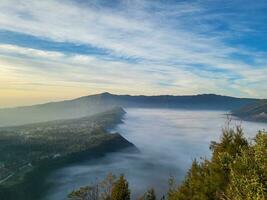 Sunrise view from Penanjakan 2 or Seruni point below can be seen as the fog begins to slowly shift to reveal a beautiful view of the sea of sand. photo