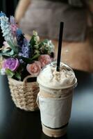 latté caramelo malteada café en tomar lejos el plastico taza y hermosa el plastico floreciente Rosa flores y flora ramo de flores en tejido rota cesta Decorar en mesa en café foto