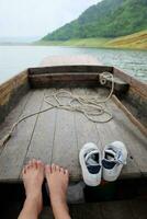 sucio y mojado mujer descalzo y zapatillas Zapatos relajante en de madera largo cola bote. viaje en Tailandia foto