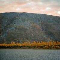 otoño paisaje en contra el antecedentes de un montaña en un del Norte río foto