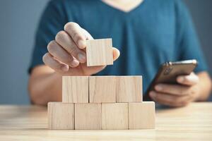 hand of a businessman stacking wood empty eight blocks with copy space for text or symbols, development concept for growth success process.and use smartphone. photo