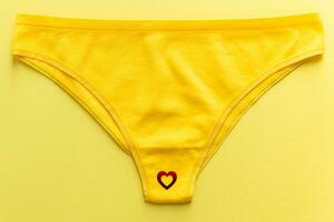 Top view of colorful females panties with red heart confetti on  yellow background photo