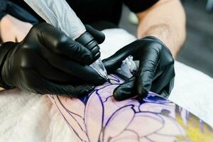 Professional tattoo artist makes a tattoo on the male leg photo