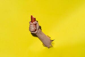 Male hand holding bitten smoked salami sausage, yellow background photo