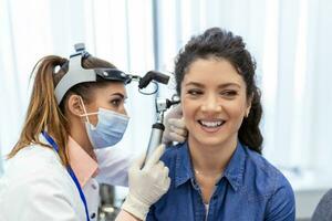 Hearing exam. Otolaryngologist doctor checking woman's ear using otoscope or auriscope at medical clinic. Otorhinolaryngologist pulling ear with hand and looking at it with otoscope closeup. photo