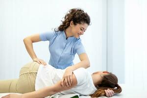 Young doctor chiropractor or osteopath fixing lying womans back with hands movements during visit in manual therapy clinic. Professional chiropractor during work photo