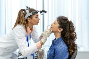 ENT clinic. Professional female doctor otorhinolaryngologist doing nose examination. Nasal congestion, sinusitis, allergy concept. Otolaryngologist examines woman's nose with nasal dilator. photo