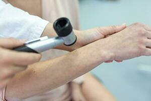 Dermatology. Skilled female dermatologist using a professional dermatoscope while doing the skin examination. Examination and diagnosis of skin diseases-allergies, psoriasis, eczema, dermatitis. photo