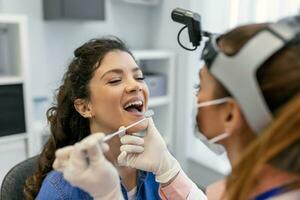 Female patient opening her mouth for the doctor to look in her throat. Female doctor examining sore throat of patient in clinic. Otolaryngologist examines sore throat of patient. photo