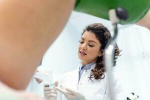 Experienced female gynecologist in lab coat, holding medical vaginal speculum for examining patient. Young woman lying on gynecological chair during check up. photo