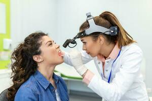 médico utilizando inspección espátula a examinar paciente garganta. ent médico haciendo garganta examen de un mujer. paciente abrió su boca a garganta chequeo foto