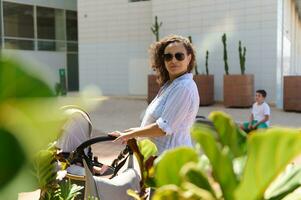 Beautiful multi-ethnic curly woman smiles and looks through her shoulders, pushing a baby pram while walking in the city photo