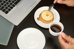 A cup of coffee and lemon tartlet on the table with partial view of laptop. Food and drink consumerism. Business concept photo