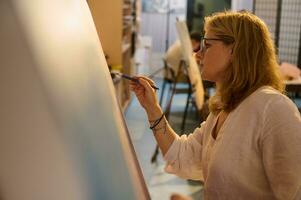 Side portrait of an authentic Caucasian female artist working on painting on canvas, in her creative art workshop photo