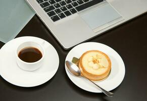 View from above of a cup of coffee, lemon tartlet and laptop on wooden table background photo