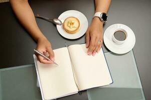 Top view woman's hand using stylish pen, taking notes on notebook, planning project, enjoying her coffee break photo