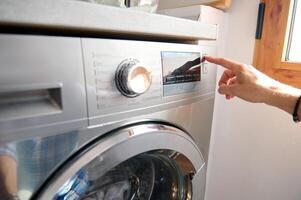 Close-up hand turning on automatic washing machine or select program with knob on control panel in white bathroom photo