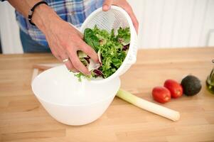 de cerca de masculino manos poniendo seco verduras y hierbas dentro un blanco cuenco mientras Cocinando sano ensalada en el hogar cocina foto