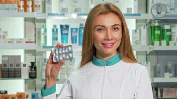 Beautiful female pharmacist smiling, holding blister of capsules at drugstore video