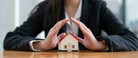 Wooden toy house protected by hands. Home insurance concept. banner ratio photo