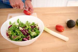 Close-up male chef chopping ripe organic tomatoes while preparing a salad from fresh organic vegetables and herbs. photo