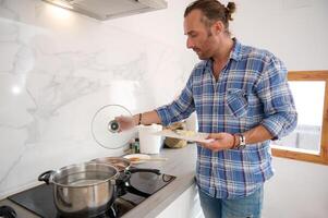 Male chef putting chopped garlic from cutting board into a saucepan with boiling tomato sauce, preparing dinner photo
