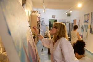 Side portrait of a creative mature blonde woman working on painting at her art studio. Education. Creative occupation photo