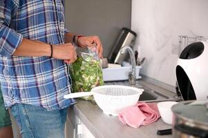 Close-up view of a male chef opening a bag with fresh herbs, standing at a table at home photo