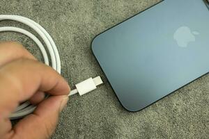 Bangkok, Thailand - October 15, 2023 Man connects usb type c cable to iPhone 15 Pro blue Titanium. Type C wired Charger. photo