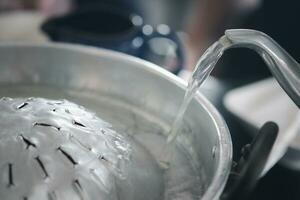 Pour water or soup from kettle to hot pan of cooking food ready for grill on the stove photo