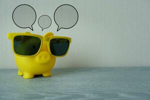 Yellow piggy bank with yellow sunglasses and speech bubble on top. Space for your individual text. photo