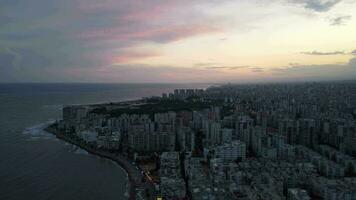 Sunset over ocean waves washes over the sandy beach of a Mediterranean city. video