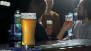 Selective focus on a beer glass, people drinking at the pub on the background video