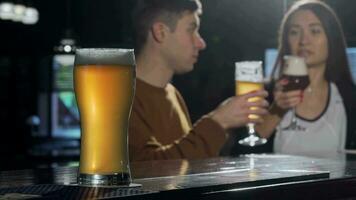 Glass of tasty beer on foreground, couple clinking beers on the back at the pub video