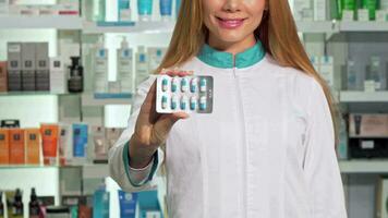 Smiling female pharmacist holding out blister of pills to the camera video