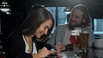 mooi gelukkig vrouw gebruik makend van haar slim telefoon, drinken bier met vrienden video