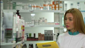 jovem fêmea farmacêutico caminhando dentro a Drogaria, verificação produtos dentro uma Lista video