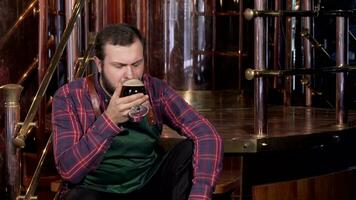 Professional brewer in apron resting after work, drinking beer of own production video