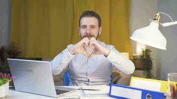 Home office worker man makes heart symbol looking at camera. video