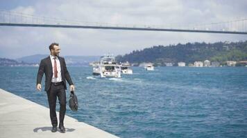 Happy and smiling businessman. He is walking on the Bosphorus in the city. video