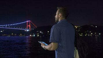 Man using tablet near illuminated bridge in strait. video