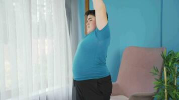 Obesity boy doing stretching exercises in front of the window. video