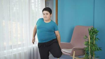 Obesity boy doing leg exercises in front of the window. video