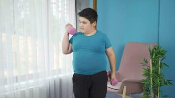 Obesity boy working out weights with dumbbells in front of the glass. video