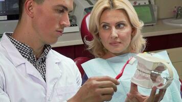 manlig tandläkare som visar hans patient på vilket sätt till borsta tänder på en käke forma video