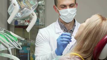 masculino dentista vestindo médico mascarar examinando dentes do fêmea paciente video